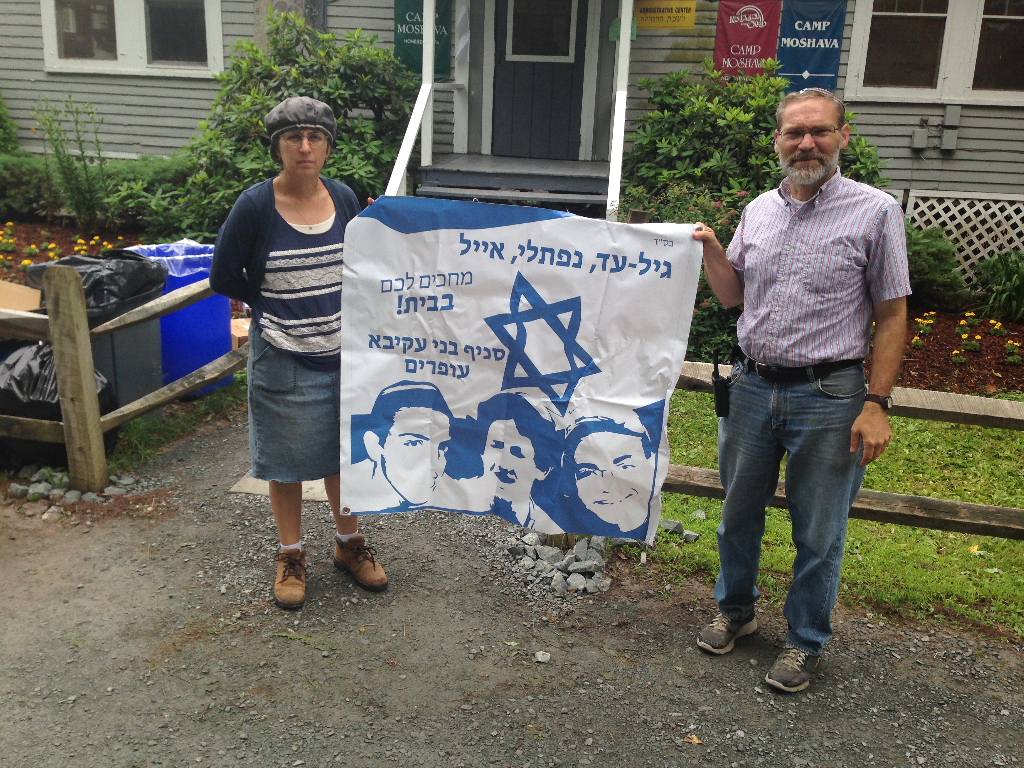 Camp Moshava's director, Alan Silverman, and its head counselor, Chanah Spiegelman, pose at the camp in Honesdale, Pa., with a banner expressing hope for the return home of three teenage Israelis who later were found to have been murdered. (Camp Moshava)