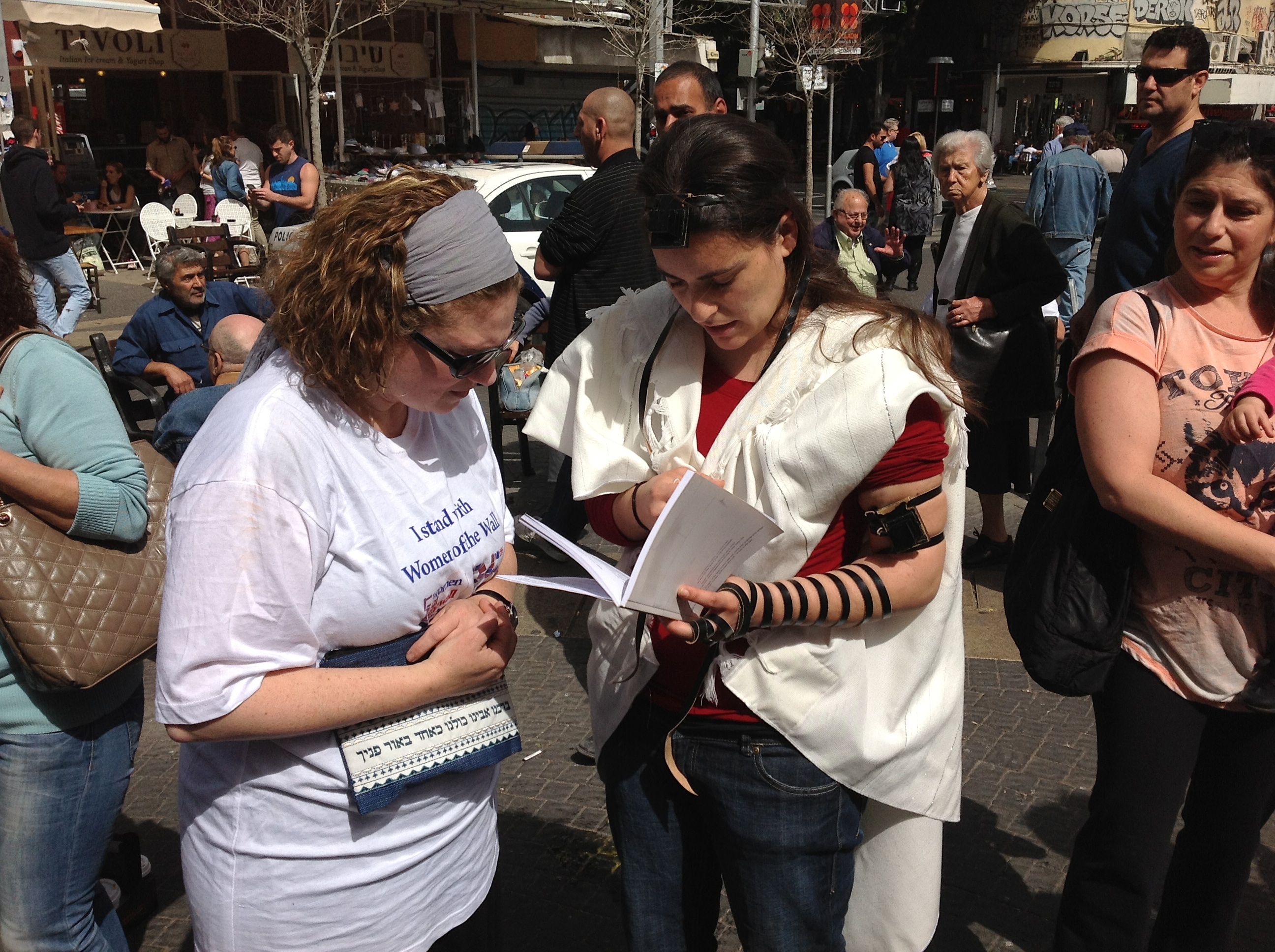 A woman lays tefillin at the entrance to Tel Aviv's Carmel Market. Women of the Wall offered women in Tel Aviv the chance to put on a tallit or tefillin on Friday. (Ben Sales/JTA)