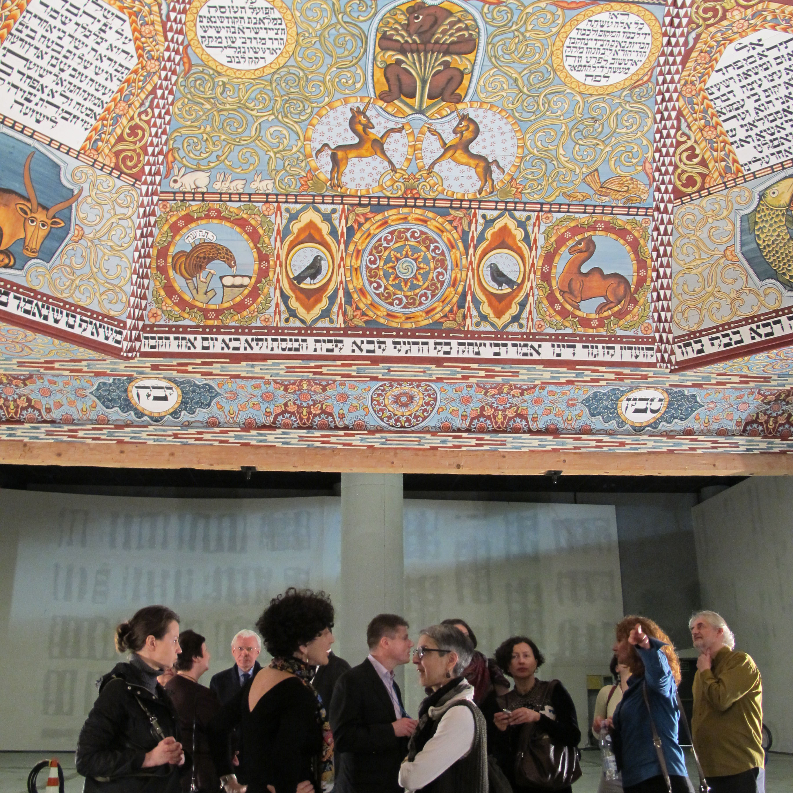 Visitors standing under the painted reconstruction of the ceiling of the Gwozdziec synagogue.