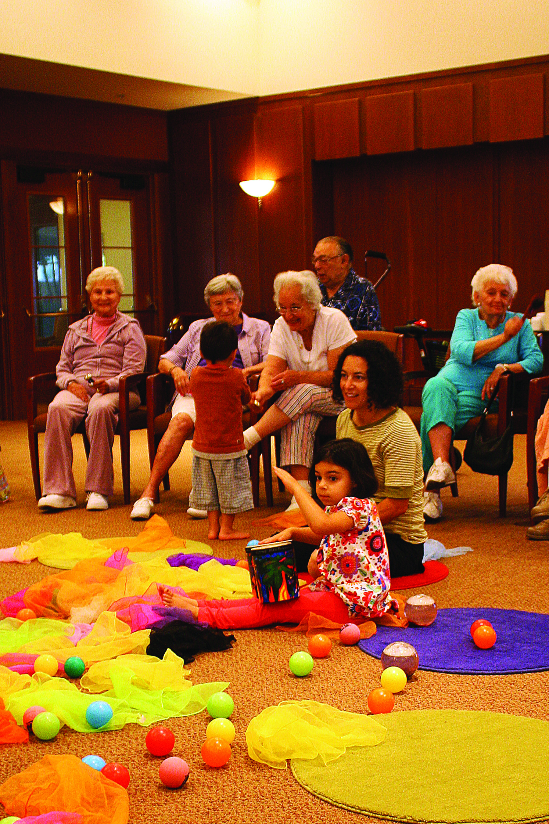 Maddie Garfinkle, 4, plays the drum at a Yad b’Yad session at the Rose Schnitzer Manor at Cedar Sinai Park in Portland, Ore., as her mom, Ali, looks on and her brother, Ian, 2, shares an instrument with his grandmother, Annette Gerard. Other Rose Schnitzer Manor residents look on. ( Peter Korchnak, Cedar Sinai Park)