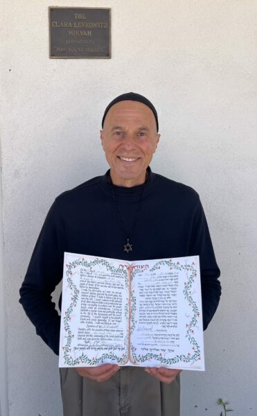 A mddle aged man wearing a kippah holds his certificate of conversion to Judaism.