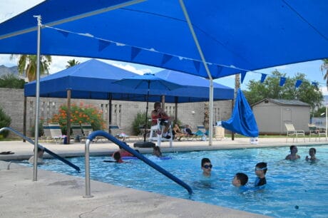 A lifeguard watches over a shaded pool where children are swimming.