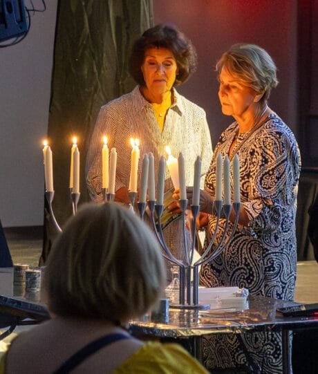 Two women light a candle on a candelabra.