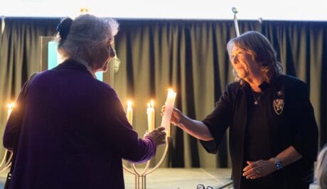 Two women pass one another a lit candle.