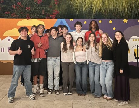 A group of teens poses before a painted wall in the courtyard of a museum.