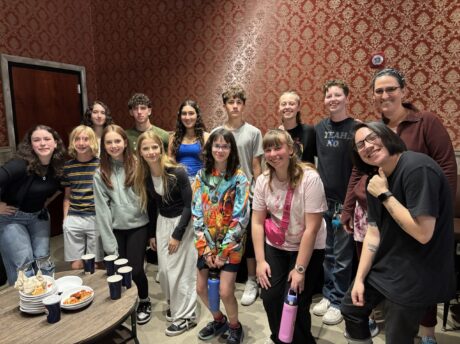 A group of teens and two adults pose inside a room at an entertainment center.