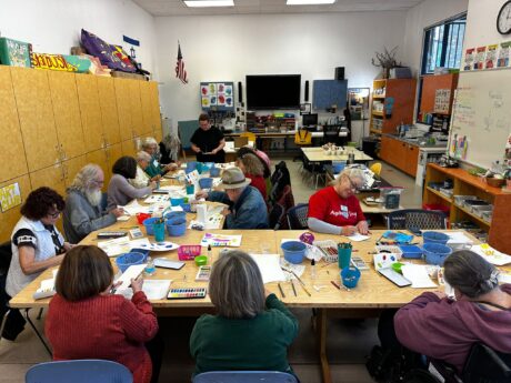 Older adults sit at tables working with art supplies.