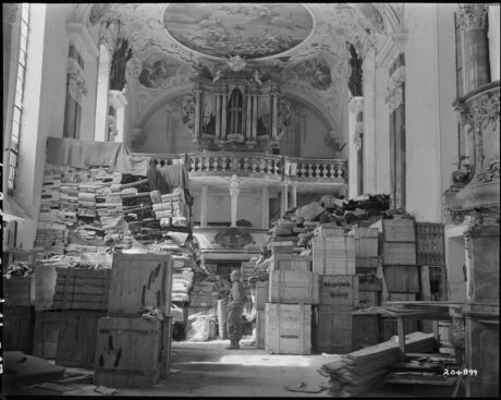 Interior of a church piled high with crates and bundles of looted items, dwarfing a soldier standing in their midst.
